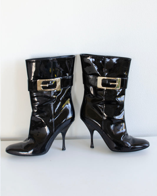 Black  Gucci patent leather stiletto ankle booties with metal buckles on a white background
